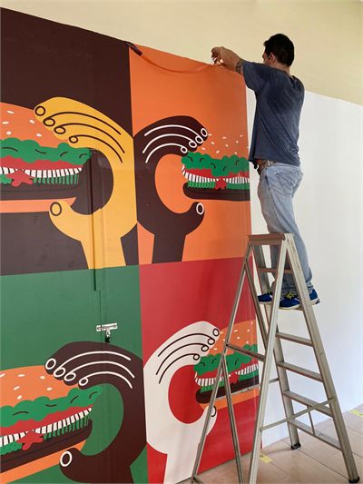 Installer on a stepladder smoothing a large printed illustrated wall graphic into place